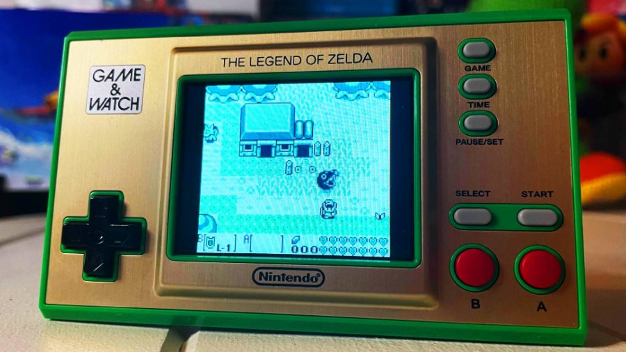 A small, green, Game & Watch shows the time and also has art from The Legend Of Zelda for Game Boy