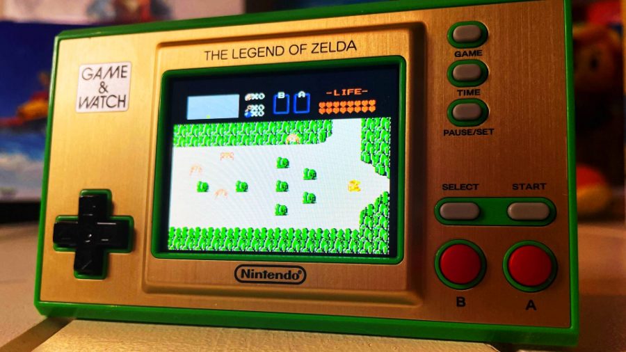 A small, green, Game & Watch shows the time and also has art from The Legend Of Zelda for NES