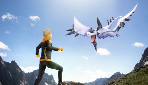 A trainer stood in the mountains with a Pokémon flying overhead