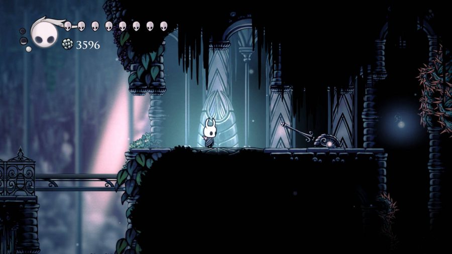 The Knight from Hollow knight walks through a dark corridor and passed a large switch 