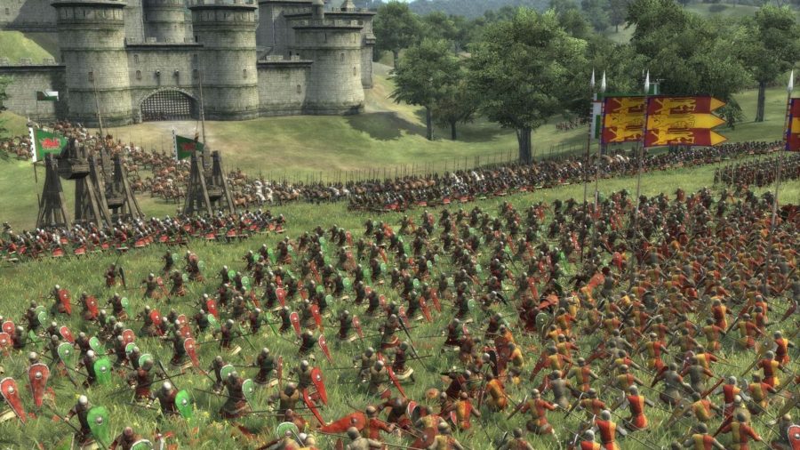 Hordes of soldiers fight in front of a castle, with trebuchets and standards high above them, in Total War: Medieval 2.