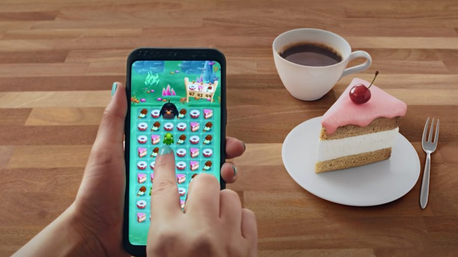 Someone playing on a phone with cake and a coffee next to them