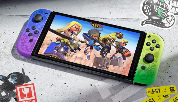 A shot of the new Splatoon 3 Switch OLED model, showing it's purple/blue and yellow/green gradient joy-con. On the screen is a shot of Splatoon 3, showing four characters preparing for battle, with yellow hair and various streetwear on. The console is on a surface with various Splatoon-themed drawings.