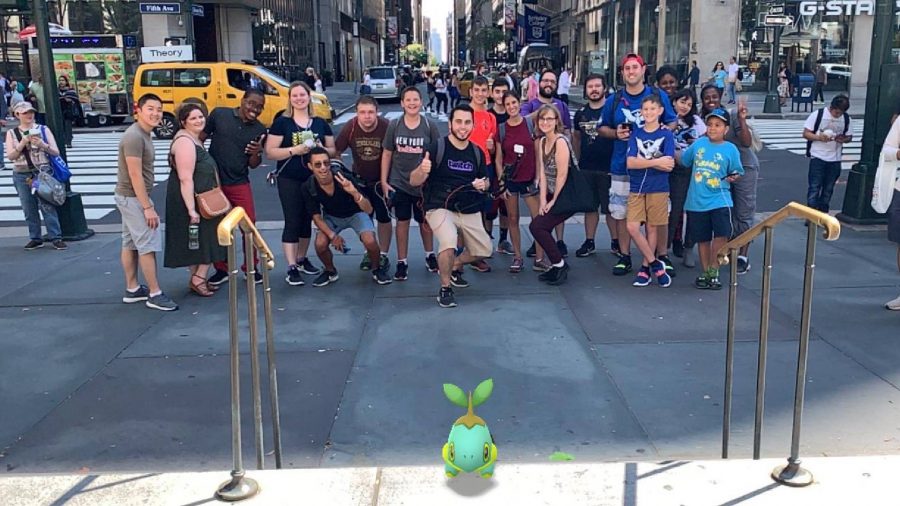 Pokemon Go sixth anniversary Niantic interview: several Pokemon Go players stand in the street posing for a photo on Pokemon Go community day, with an AR image of a shiny Turtwig in front of them
