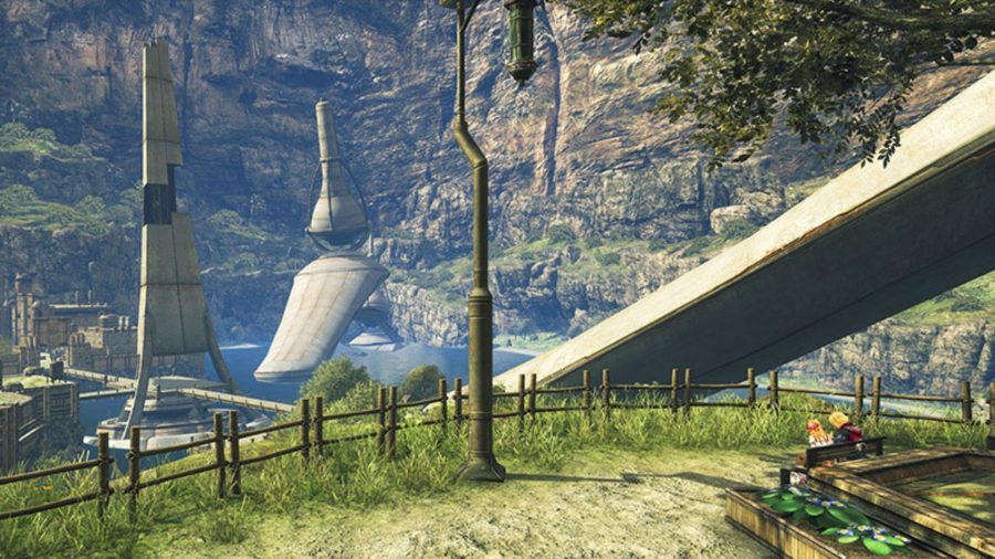 Colony 9 in Xenoblade Chronicles. In the foreground there is a patch of land with a barrier around its edge, with a bench on it and a couple of people sat on it. In the distance there are strange white buildings, cliff walls, and water.