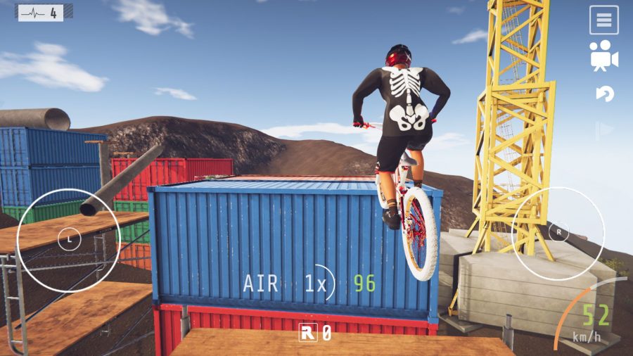 A screenshot from our Descenders mobile review showing a biker jumping off a wooden platform towards a pile of blue and red shipping containers, in a place that looks like a construction site.